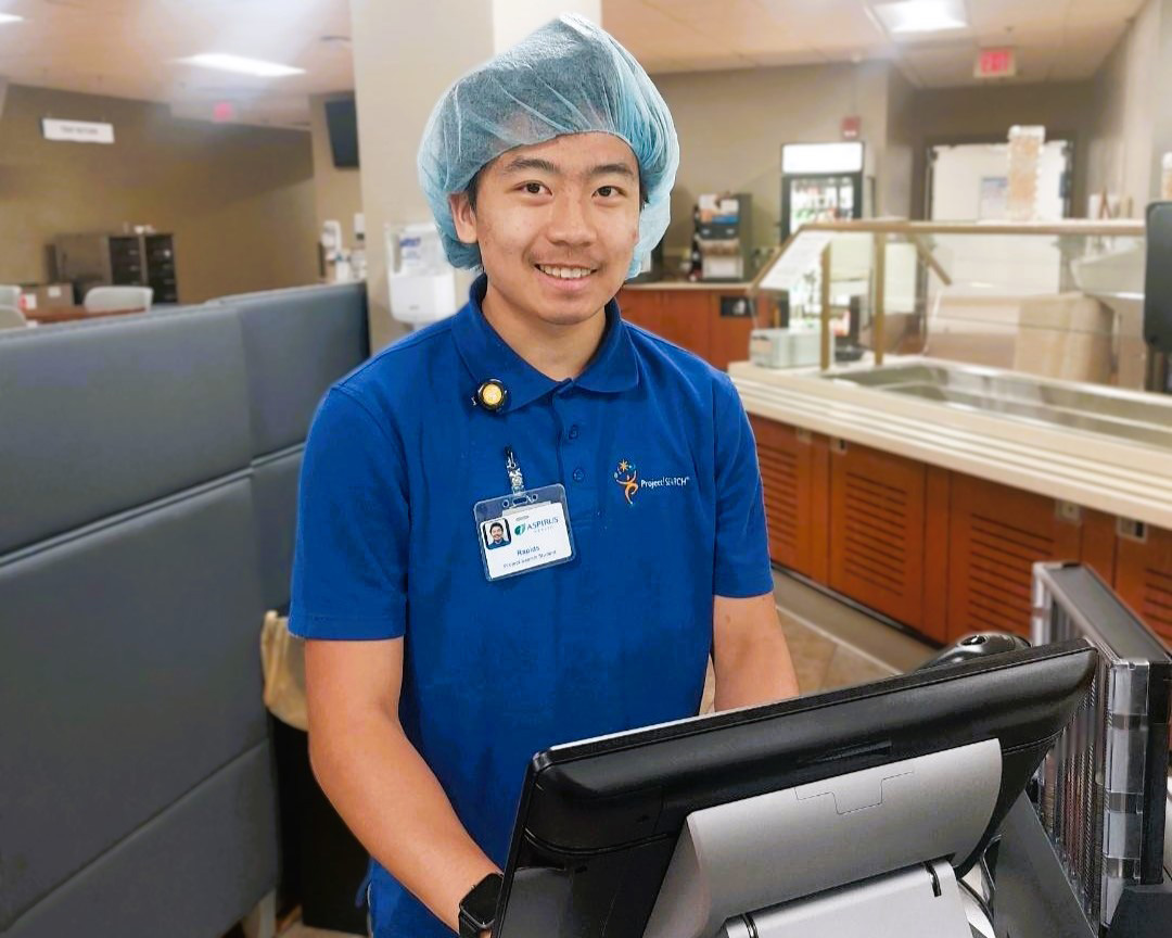 A man smiles behind a work kiosk