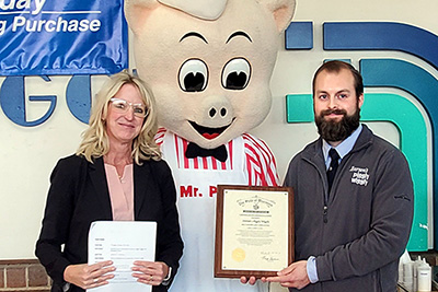store manager receiving award while Mr. Pig looks on